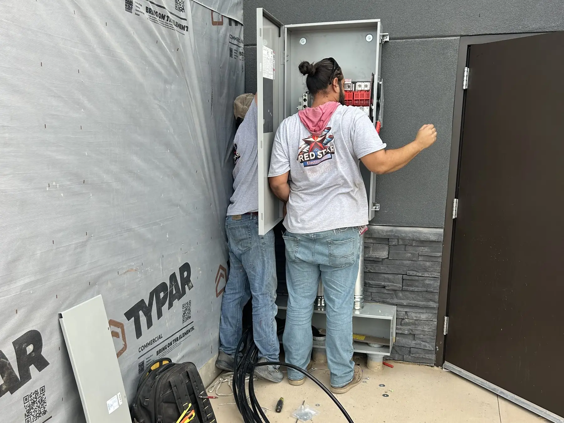 An electrician working at an open panel in a space being finished out